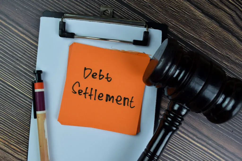 Sticky note labeled 'Debt Settlement' with a gavel on a wooden table, symbolizing legal approaches to debt resolution